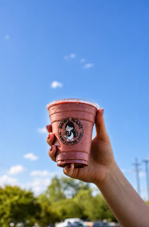 Hand holding a berry smoothie against a blue sky