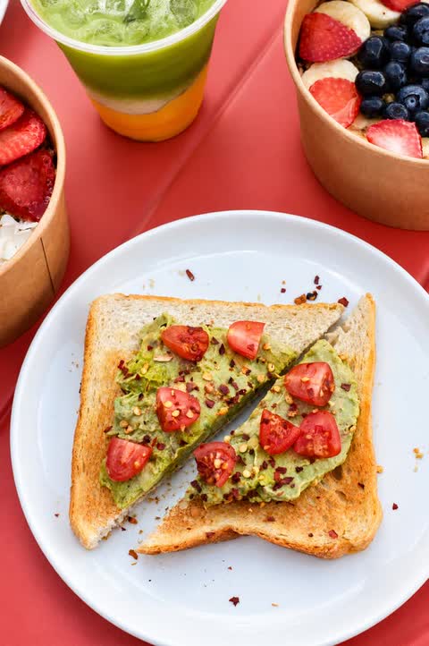 Avocado toast with tomatoes beside fruit bowls and a layered drink